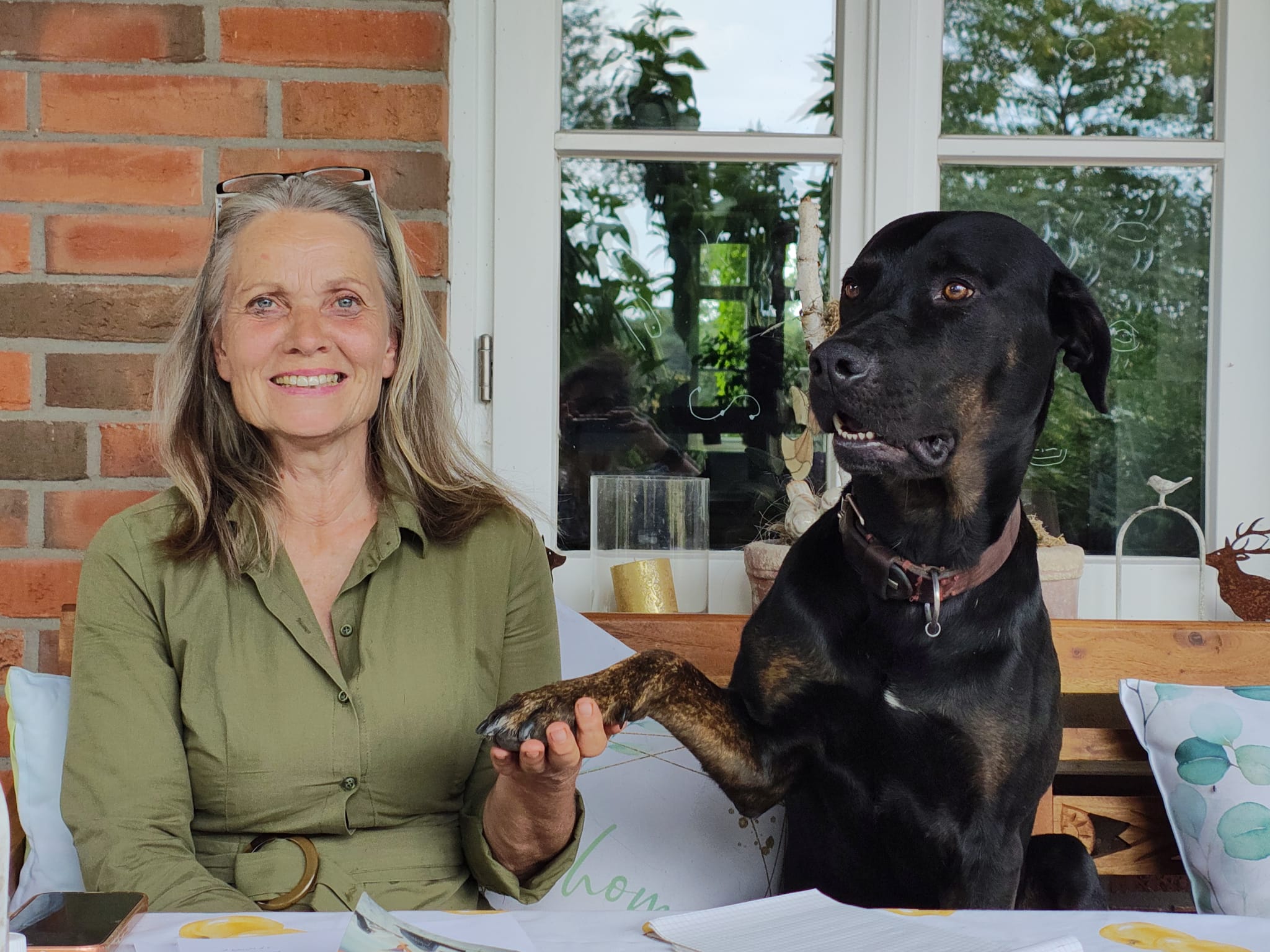 Silke Volkmann sitzt neben ihrem Hund Neo auf einer Bank und hält seine Pfote.